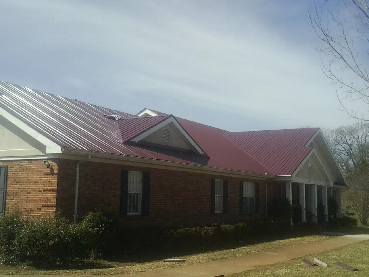 Red metal roof with gabled entries on a long brick building, from a Hail Damage Roof Repair job in Larwill