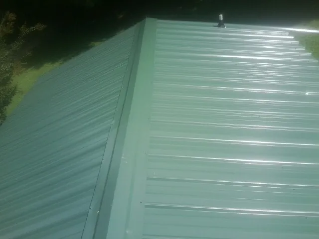 New green metal panels meeting at the ridge of a roof — Flat Roof Repair work by our crew in Larwill