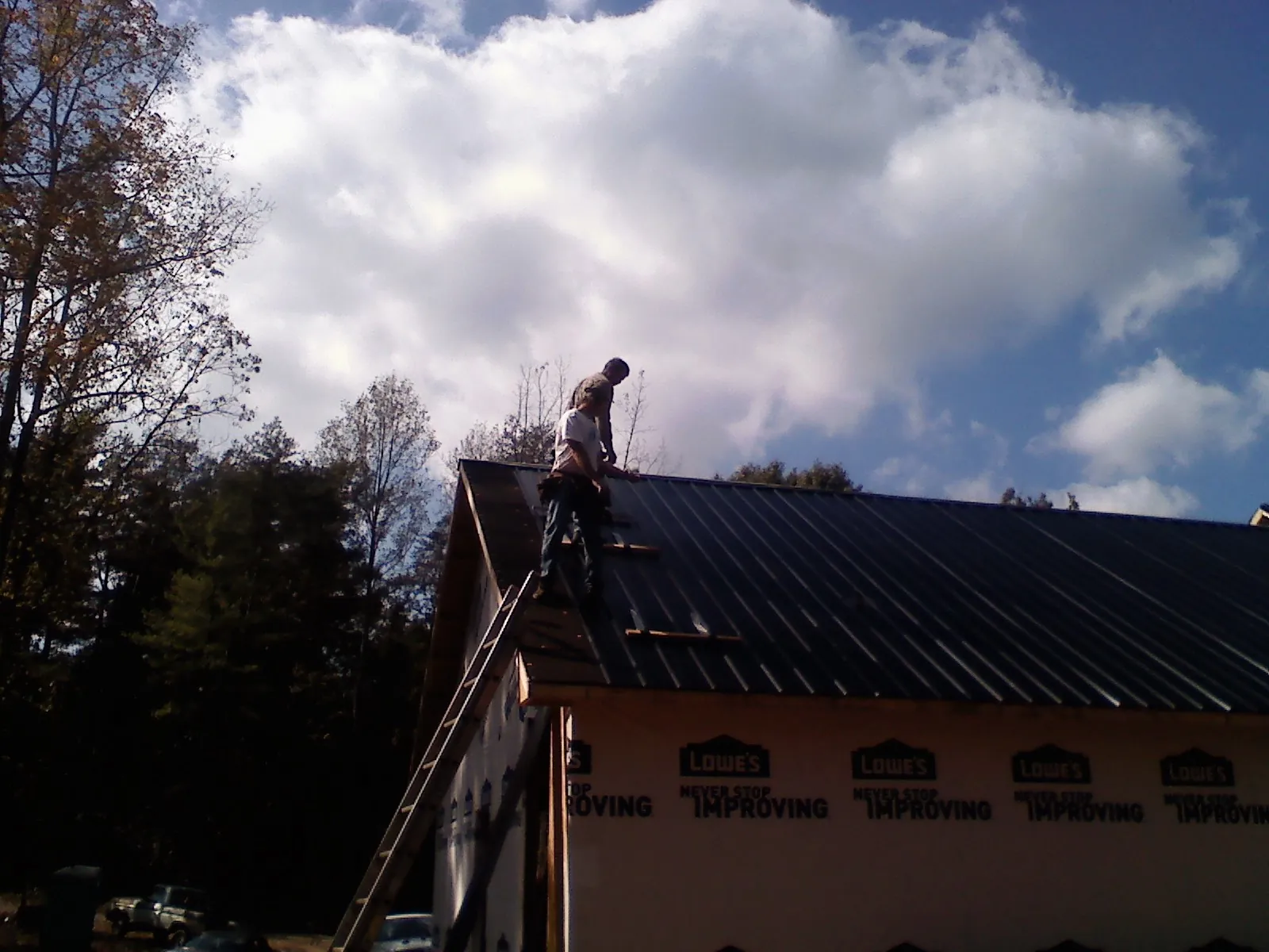 Roofer fastening dark metal panels high against a cloudy sky, from a Roof Inspection job in Larwill