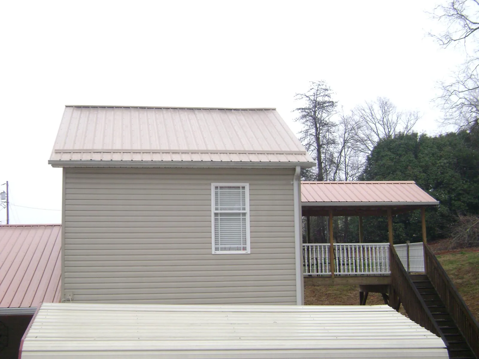 Tan metal roofs on a two story addition and attached porch, from a Roof Replacement job in Larwill
